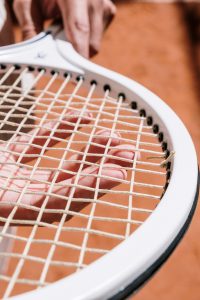 Close-Up Photo of a Person's Hand Touching Tennis Racket Strings