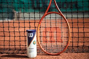 Tennis racket and ball can in front of a net on a clay court, showcasing sports equipment.